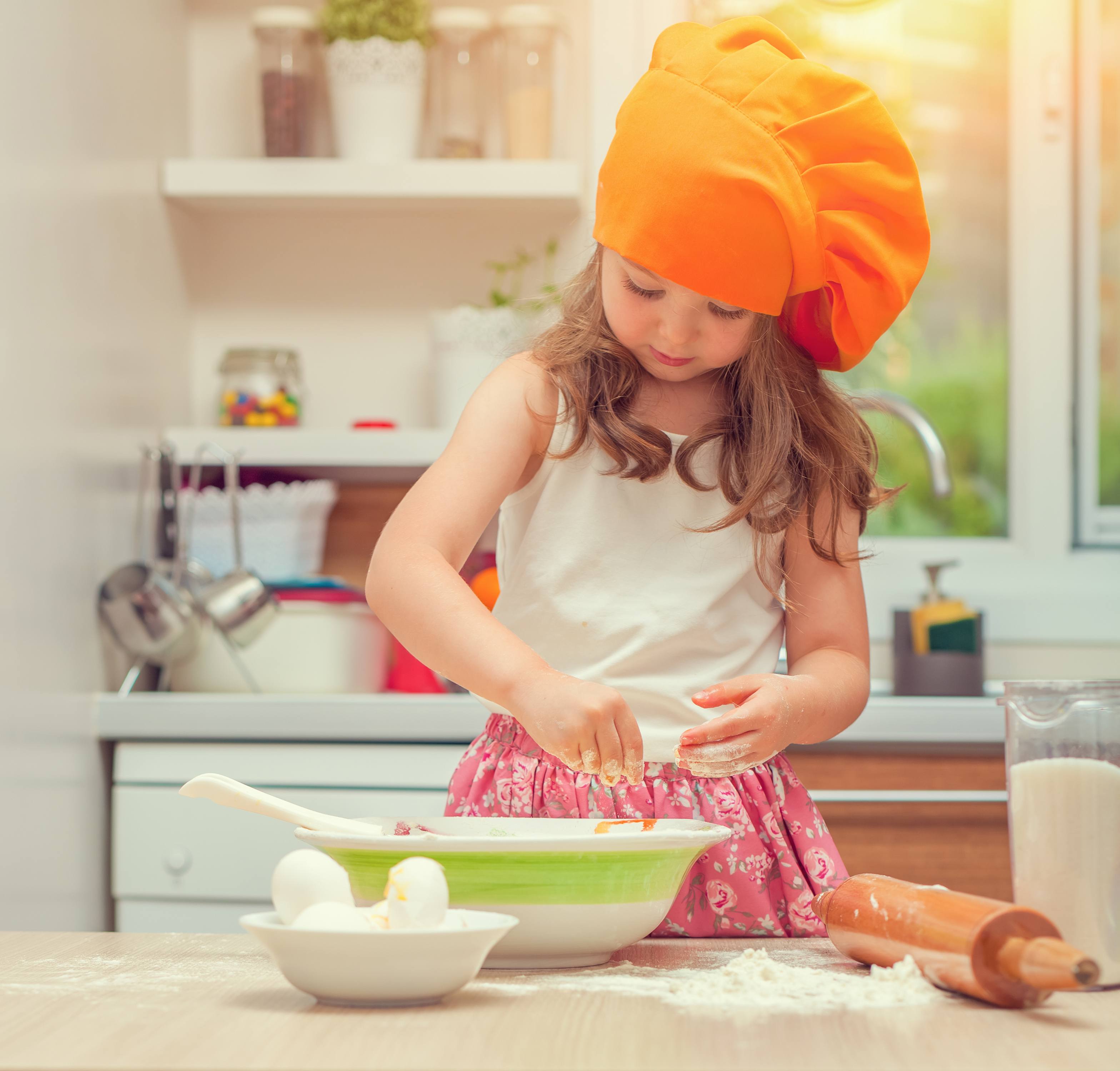 beautiful cute little girl with bonnet making pasta dough in kitchen